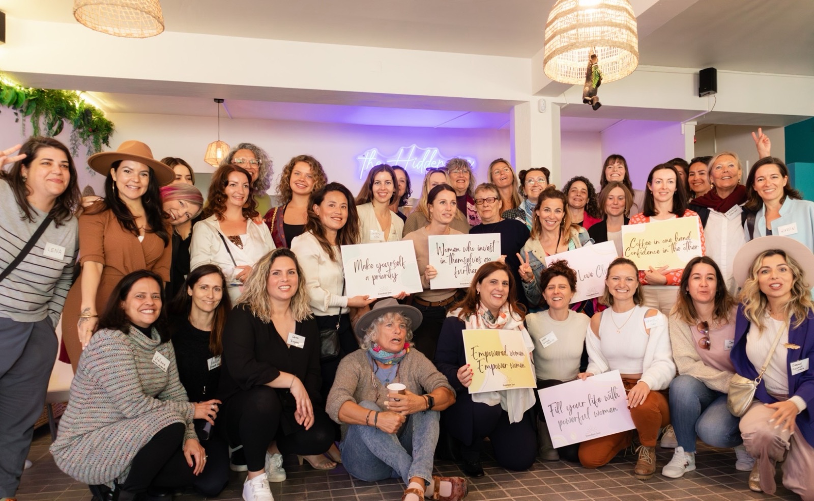 A large group of women from the Women's Money Society community smiling together and holding hand-lettered signs